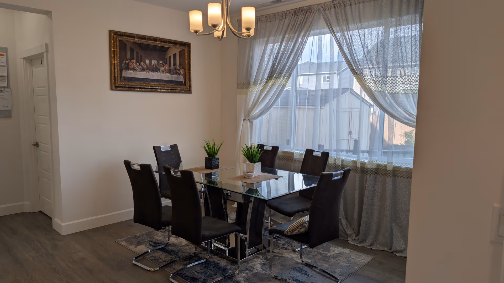 Glass dining table with black chairs in a bright, curtained dining room.