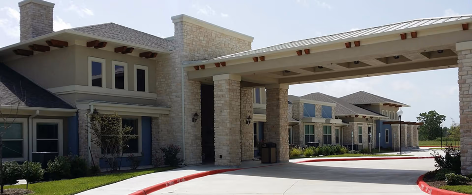Front entrance of a stone-and-stucco senior living building with a covered porte-cochère and curved driveway.