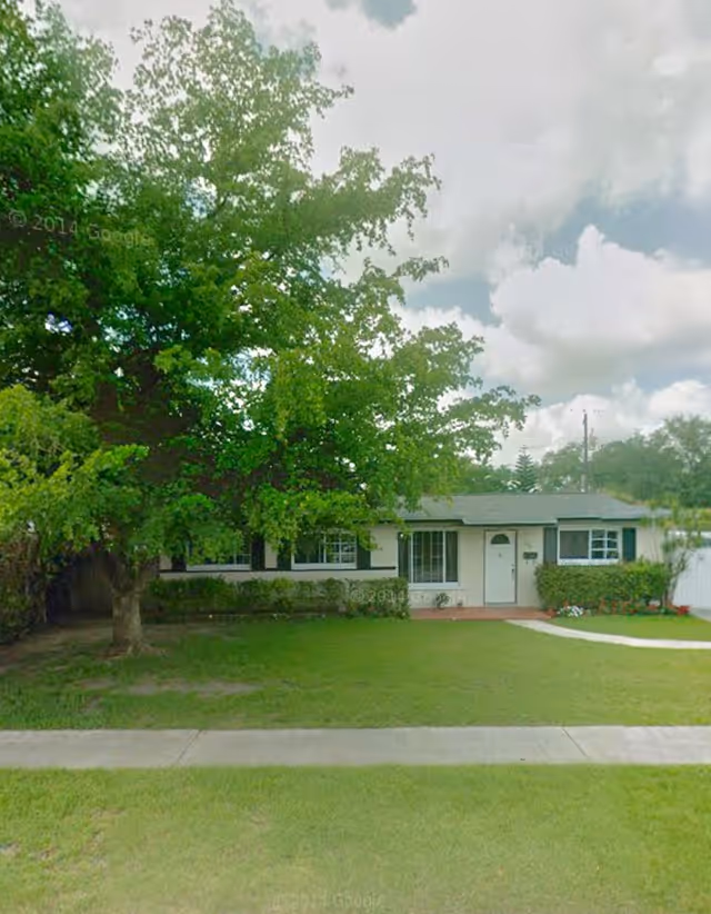 Single-story light-colored house with front yard, large tree, shrubs, and a walkway to the door.