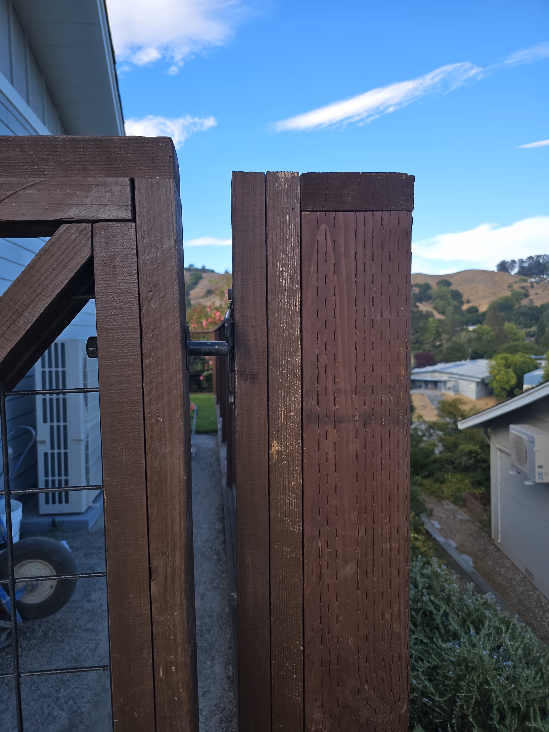 Wooden balcony railing overlooks a blue sky and hilly residential neighborhood.