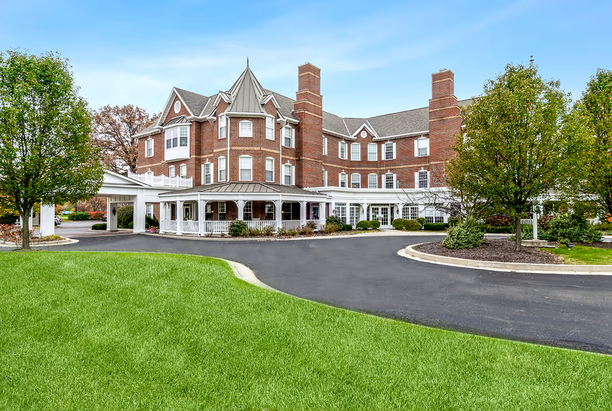 Brick-assisted living building with a long driveway, white entrance veranda, and well-kept green lawn.
