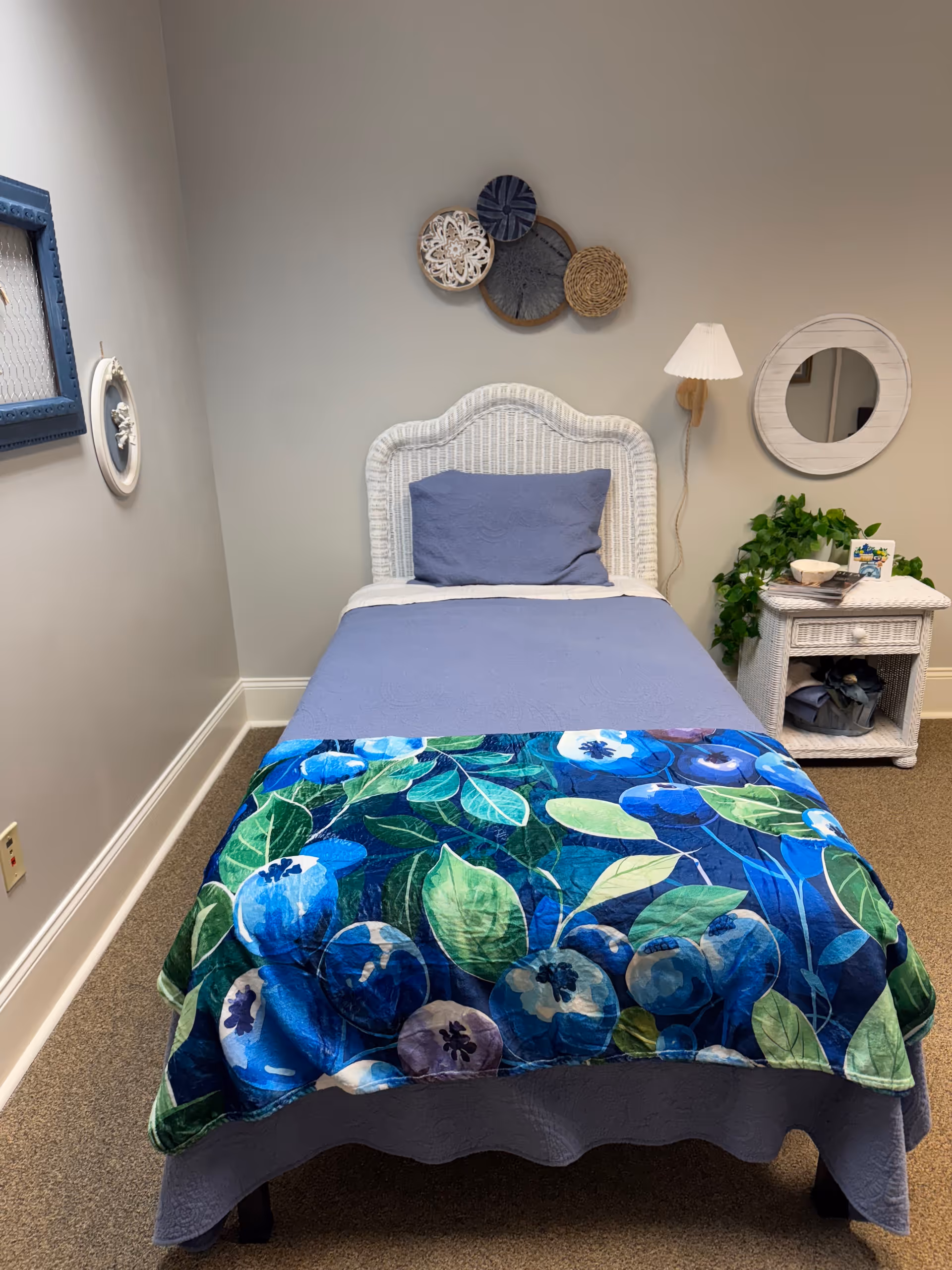 Cozy bedroom with a white wicker bed, blue bedding, wall art, lamp, and nightstand.