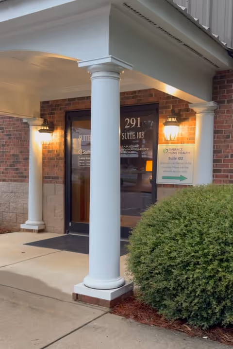 Exterior view of Embrace Home Health facility entrance with white columns and brick facade.