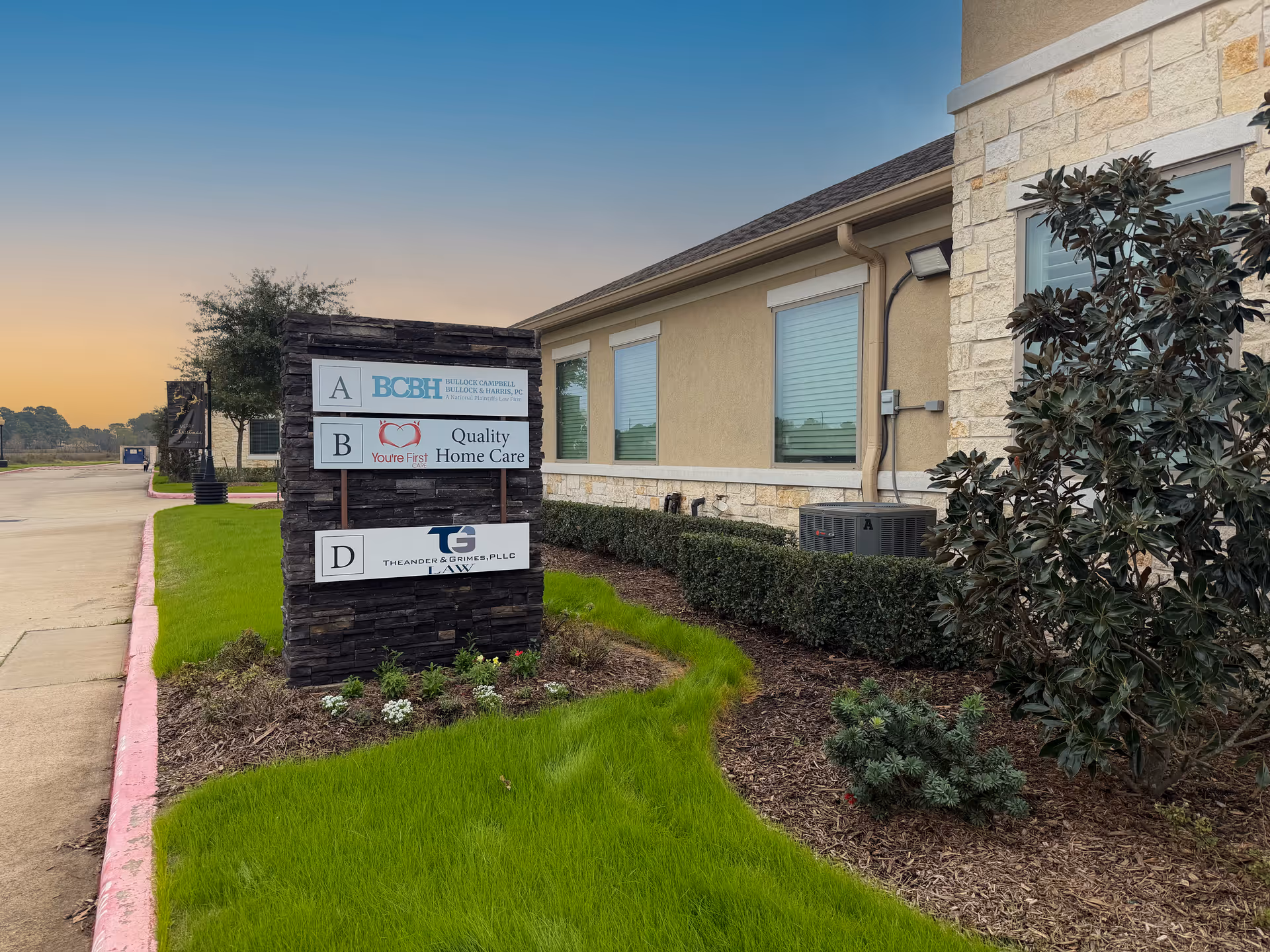 Exterior view of a senior care facility with a stone sign and landscaped front yard.