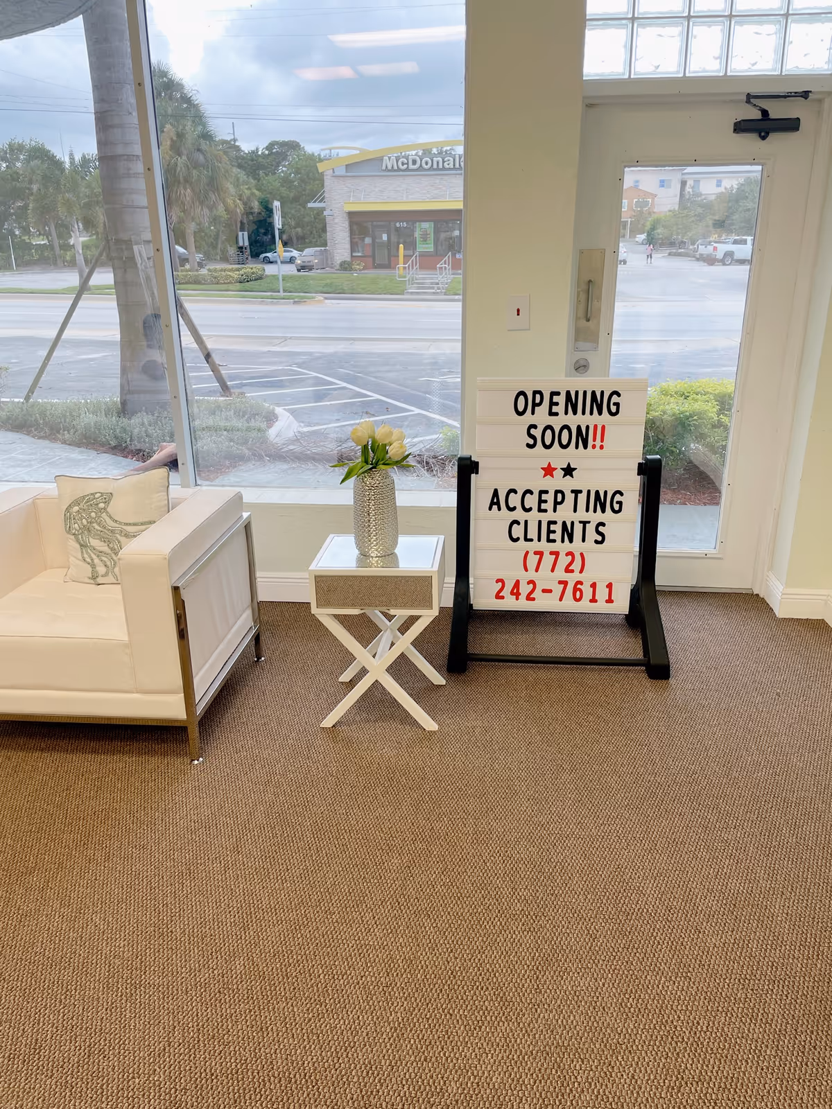 Bright lobby with white sofa, small table, vase, and an 'Opening Soon' sign.