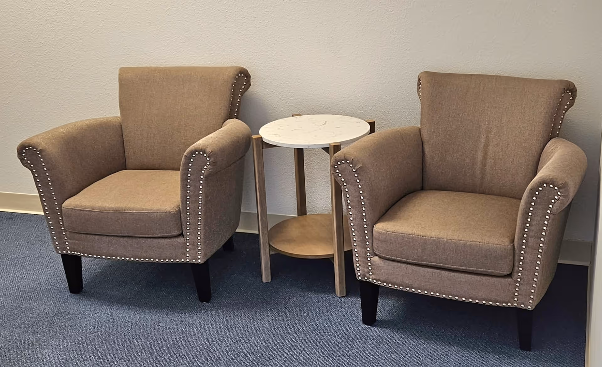 Two beige upholstered armchairs with a small round marble table between them in a lounge area