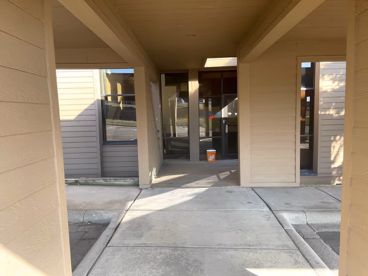 Beige senior living facility entrance with glass doors and a small orange bucket outside.