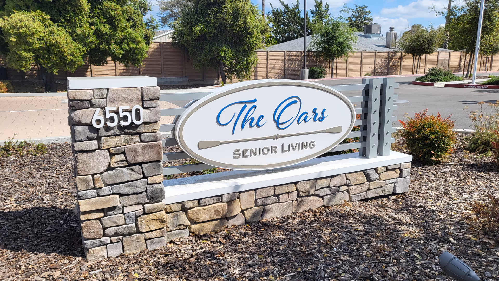 Stone entrance sign reading "The Oars Senior Living" with the address 6550 amid landscaped grounds.