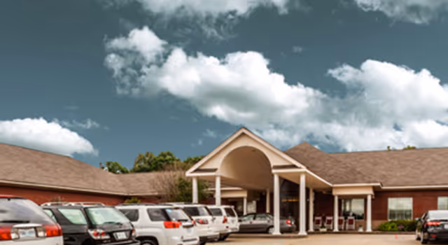 Senior living facility entrance with a covered drive and parked cars in front.