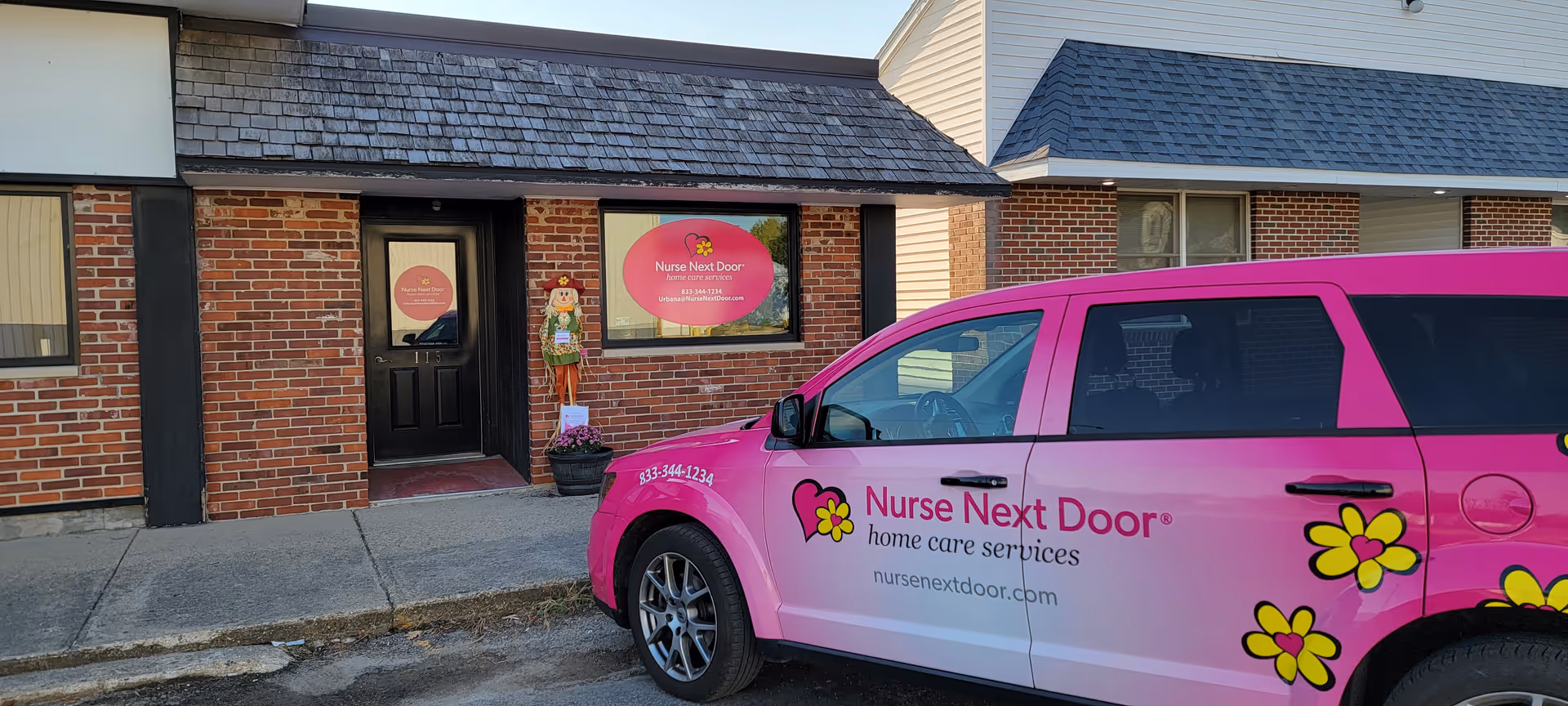 Brick building exterior with Nurse Next Door signage and a pink promotional van parked outside.
