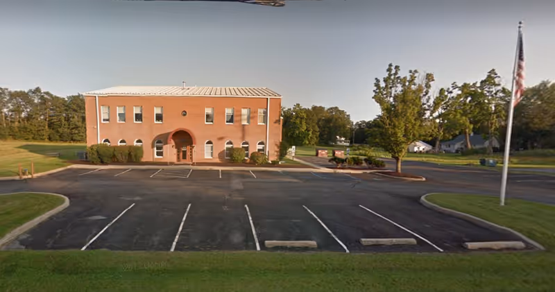 Exterior brick building with a parking lot, trees, and a flag.