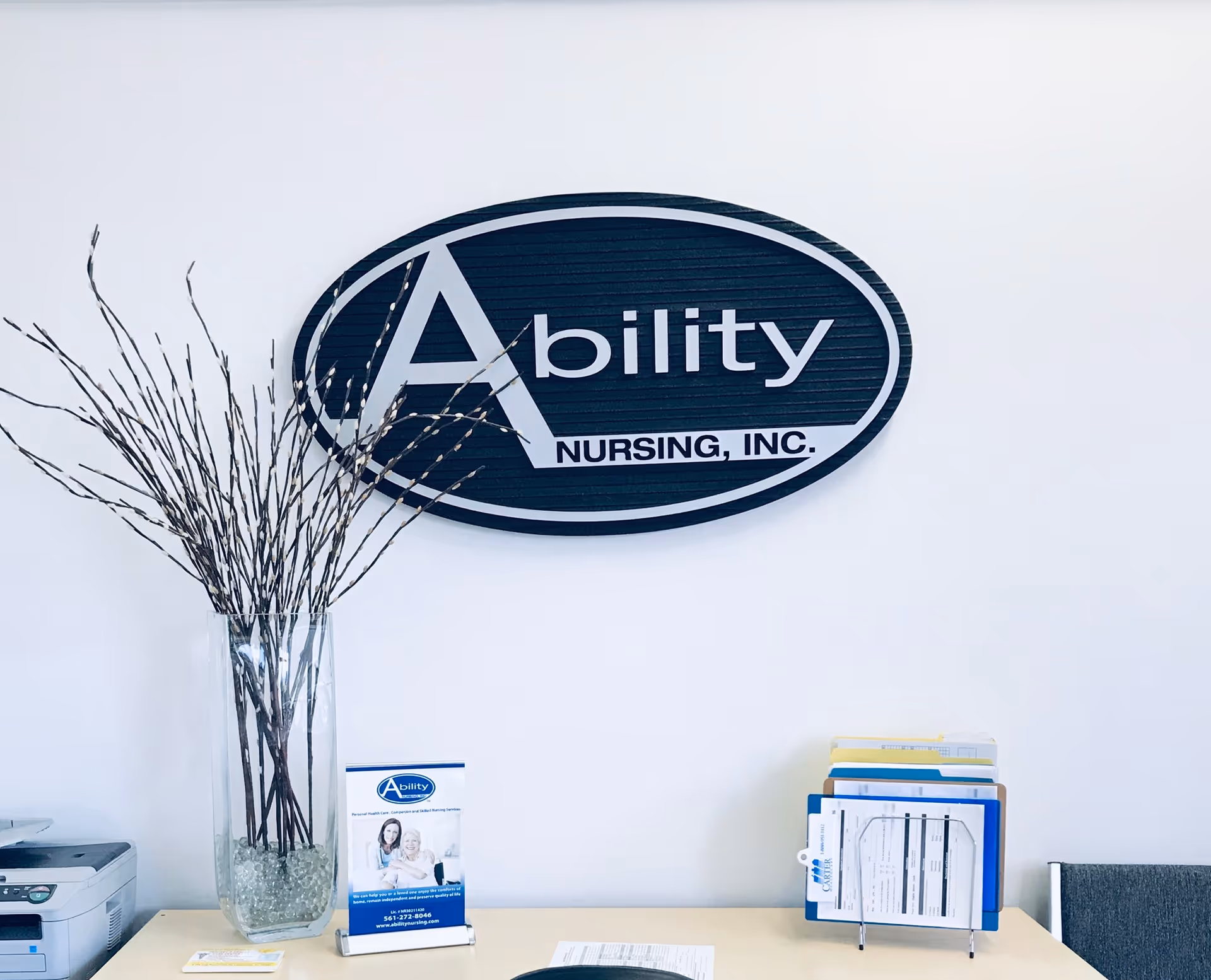 Lobby reception area featuring Ability Nursing, Inc. logo on wall with a vase and brochures.
