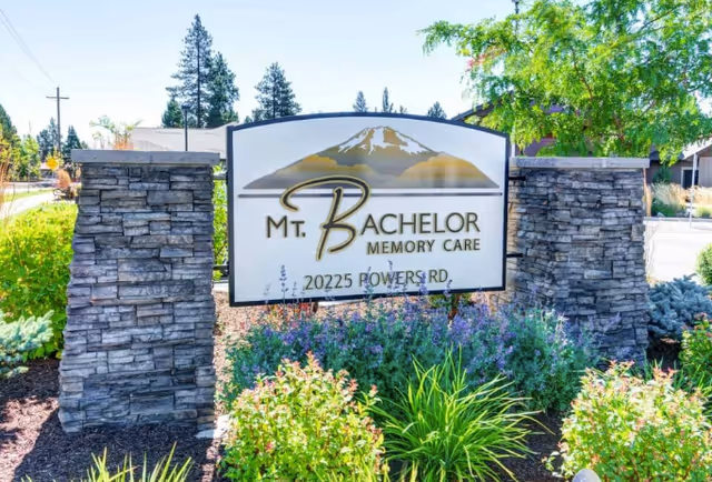 Outdoor Mt Bachelor Memory Care sign flanked by stone columns and shrubs.