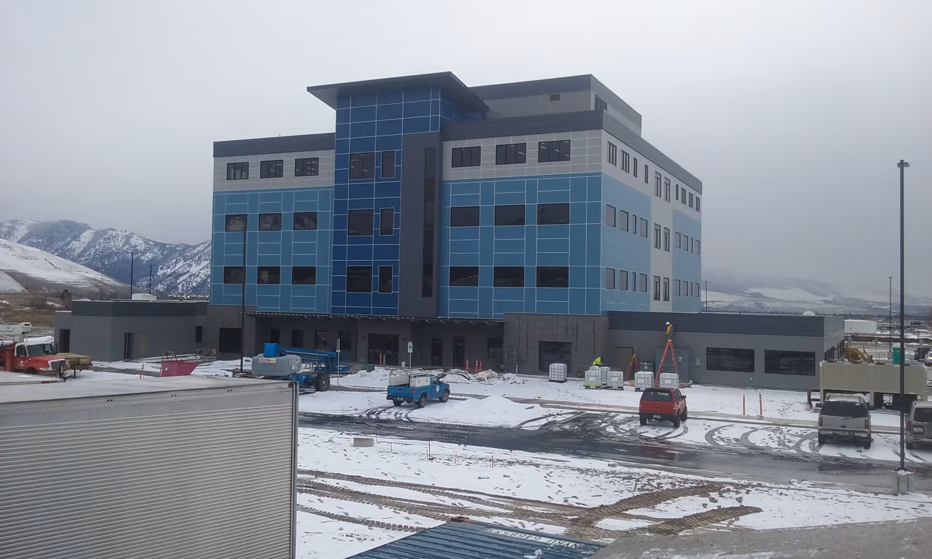 A blue, multi-story building under construction in a snowy landscape.
