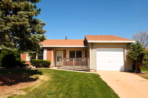 Front view of a single-story house with a small porch, attached garage, and green lawn.