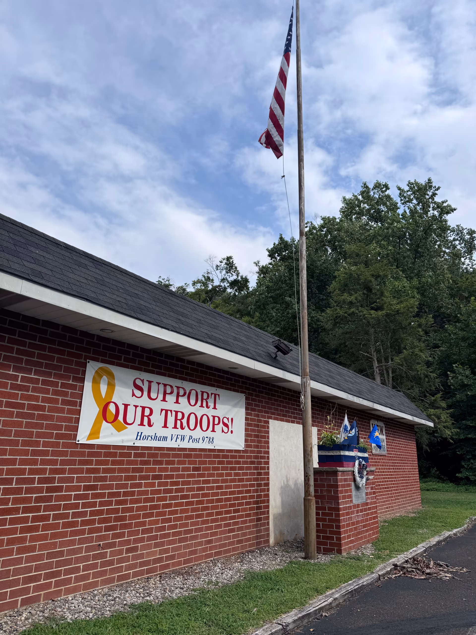 Red brick facility exterior with flagpole and 'Support Our Troops!' banner.