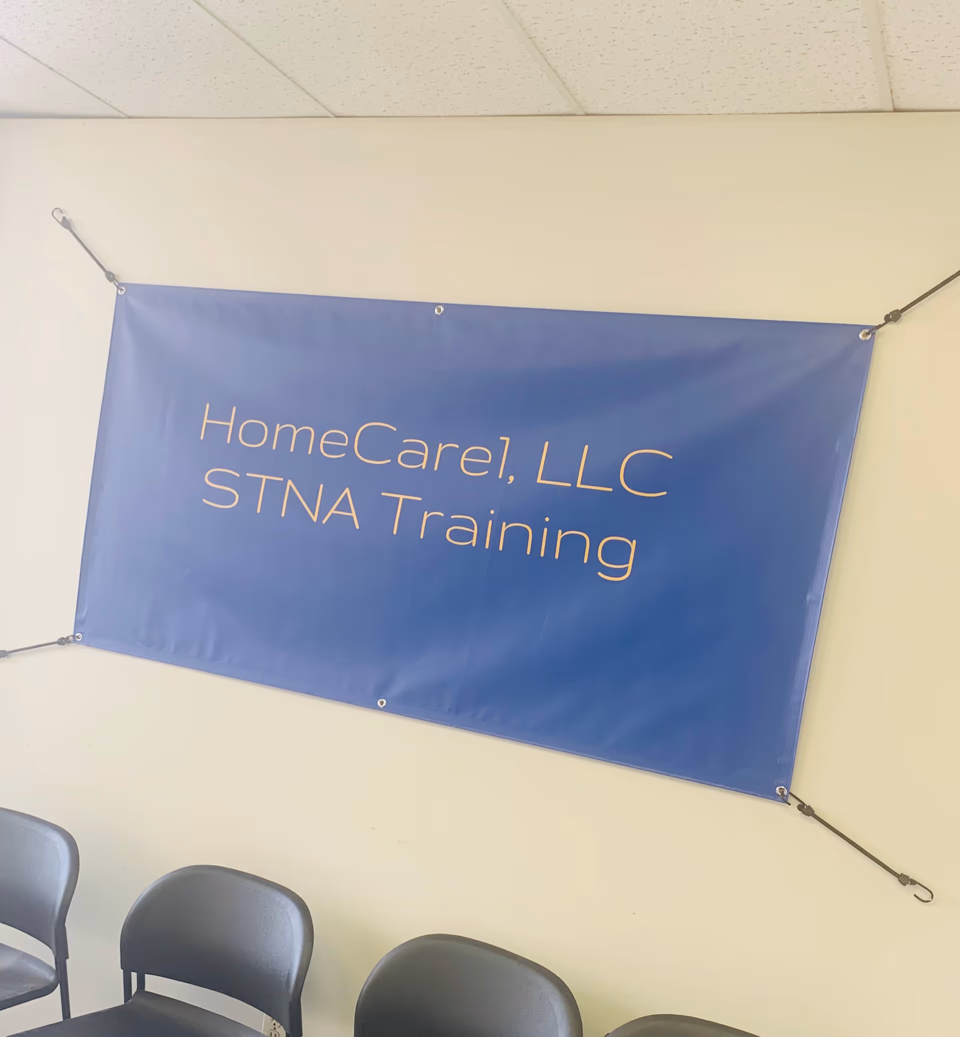 Blue banner reading HomeCare1, LLC STNA Training hangs on a wall in a classroom.