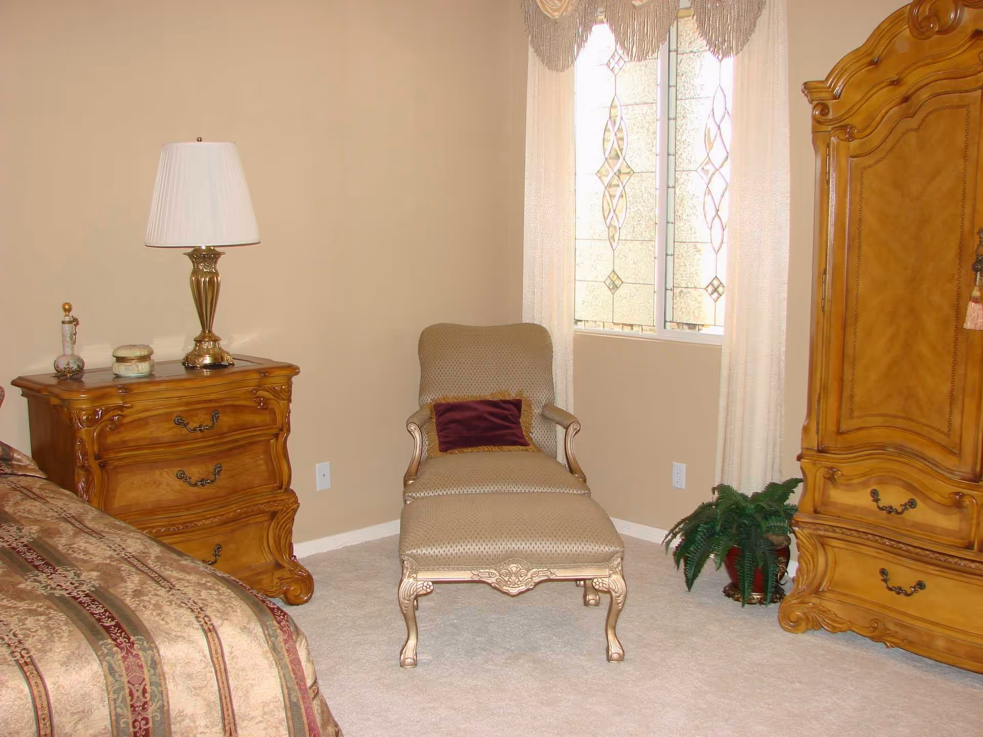 Classic bedroom with ornate wooden furniture, upholstered chair, dresser, armoire, and window.