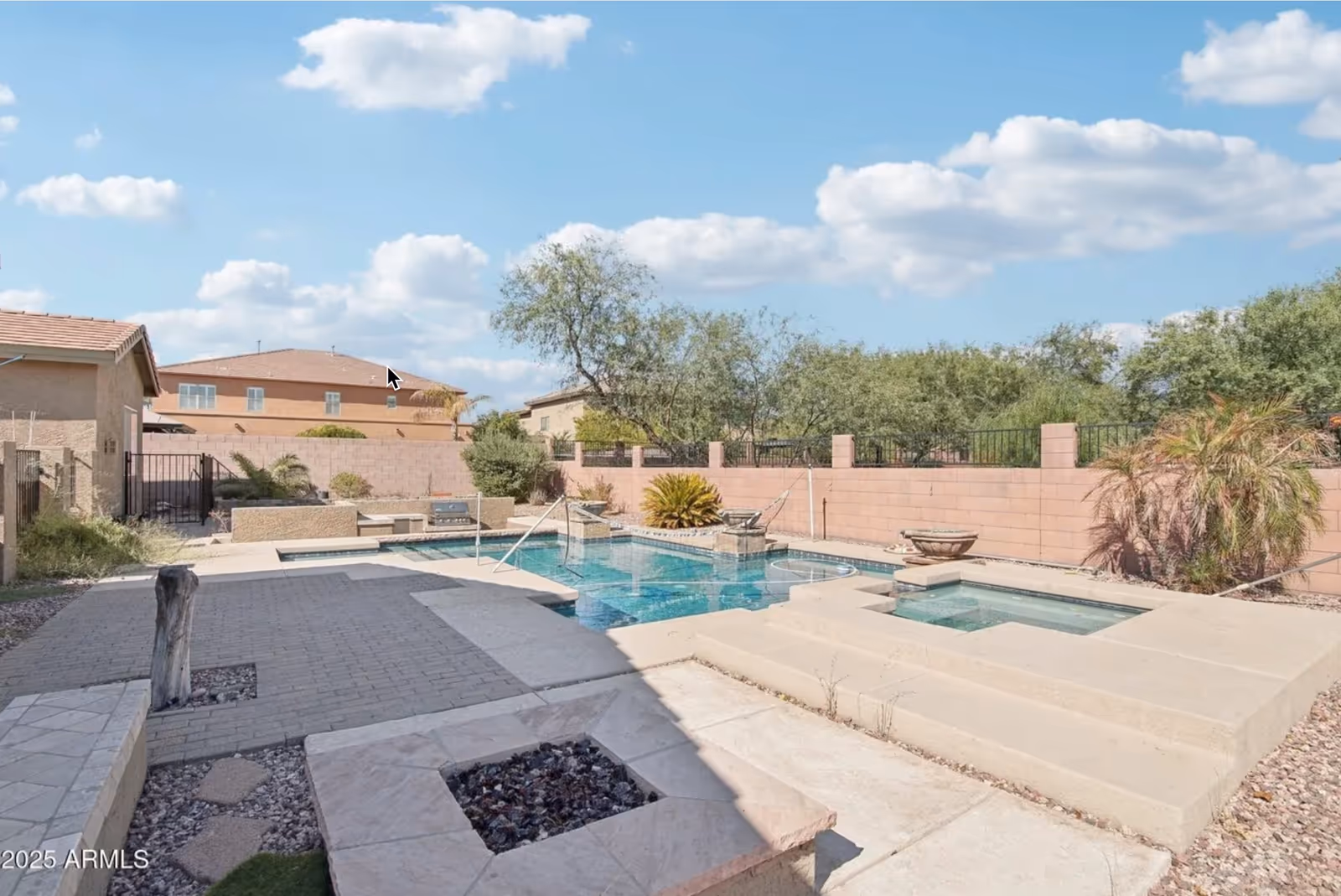 Sunny outdoor pool area with steps, seating, and brick boundary walls.