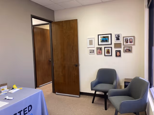 A small waiting area with two gray armchairs, a photo collage, and an open doorway.
