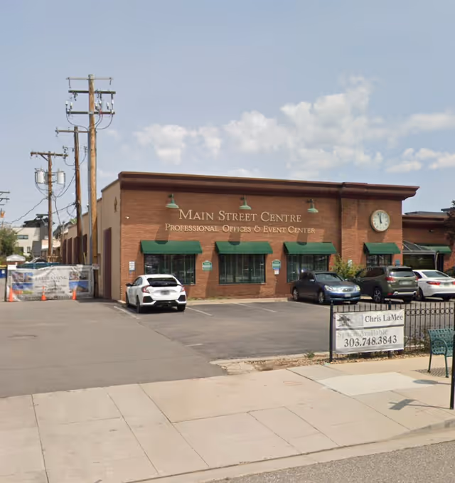 Brick building labeled Main Street Centre with green awnings and parked cars.