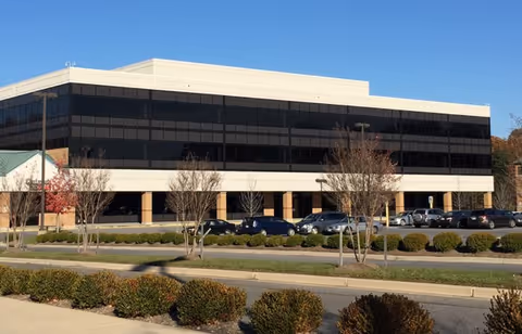 Exterior view of a modern glass-front building with a parking lot.
