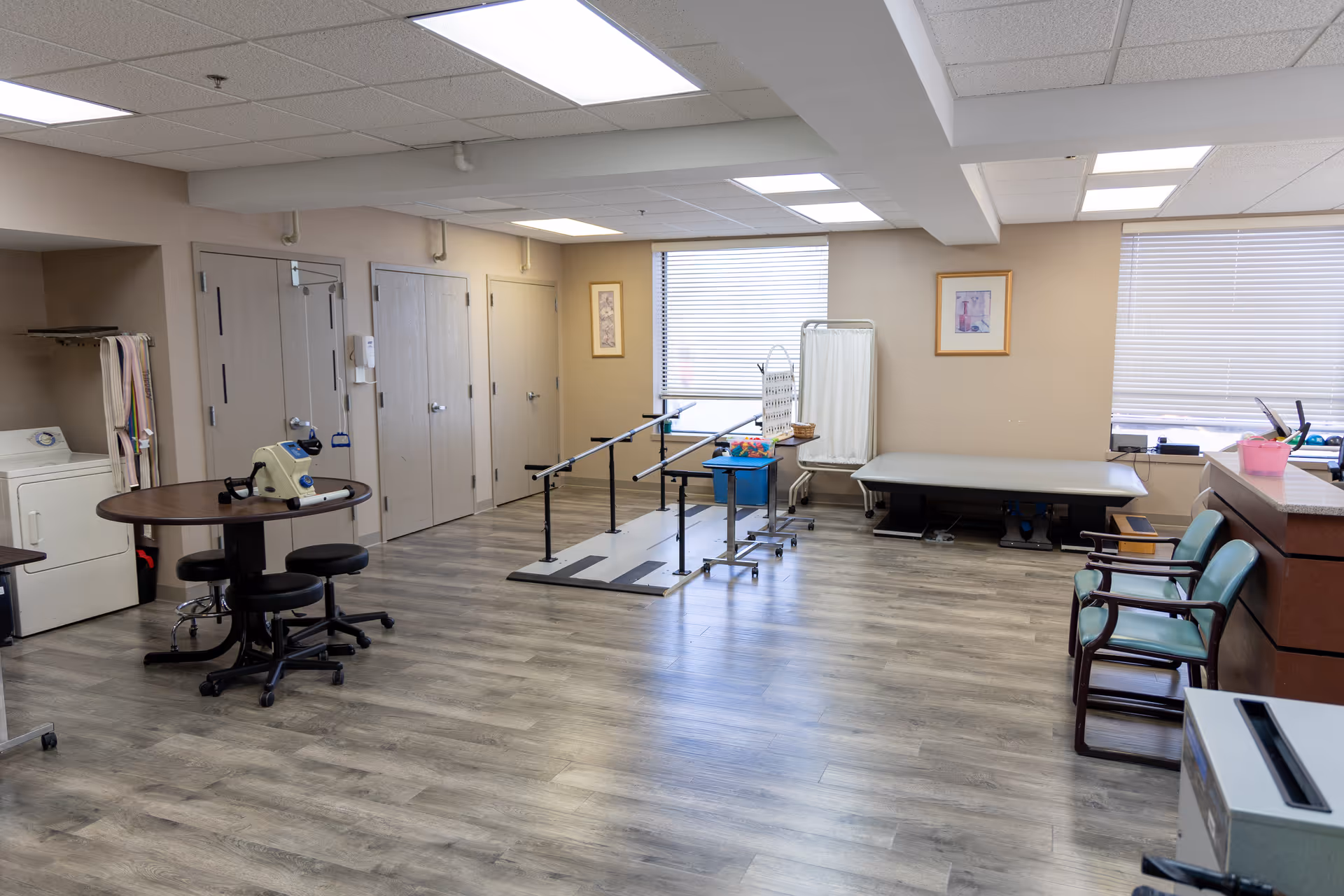 Rehabilitation room featuring parallel bars, a treatment bed, exercise equipment, and seating.