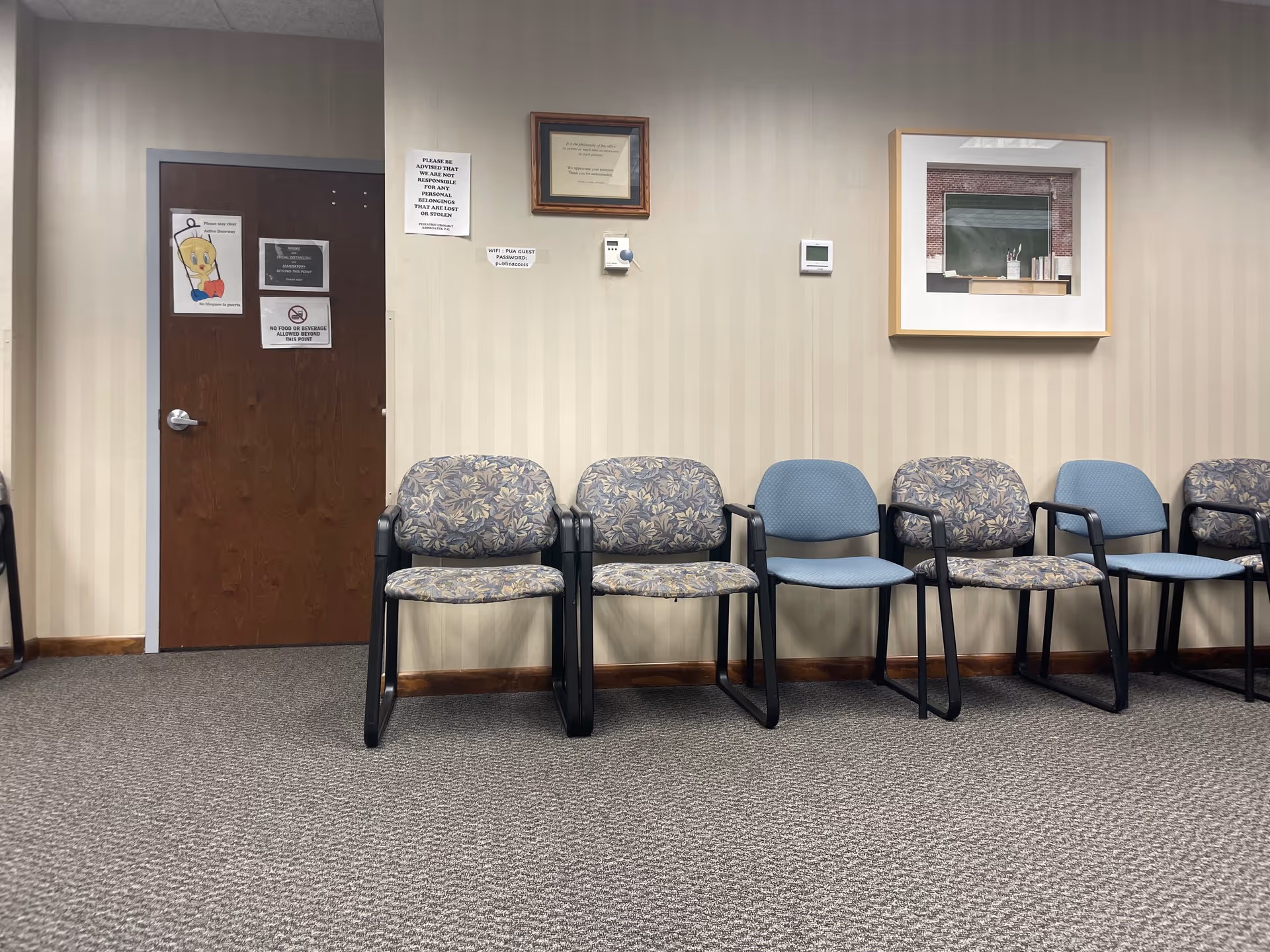 Row of blue and patterned chairs line a beige-striped wall in a clinic waiting area.