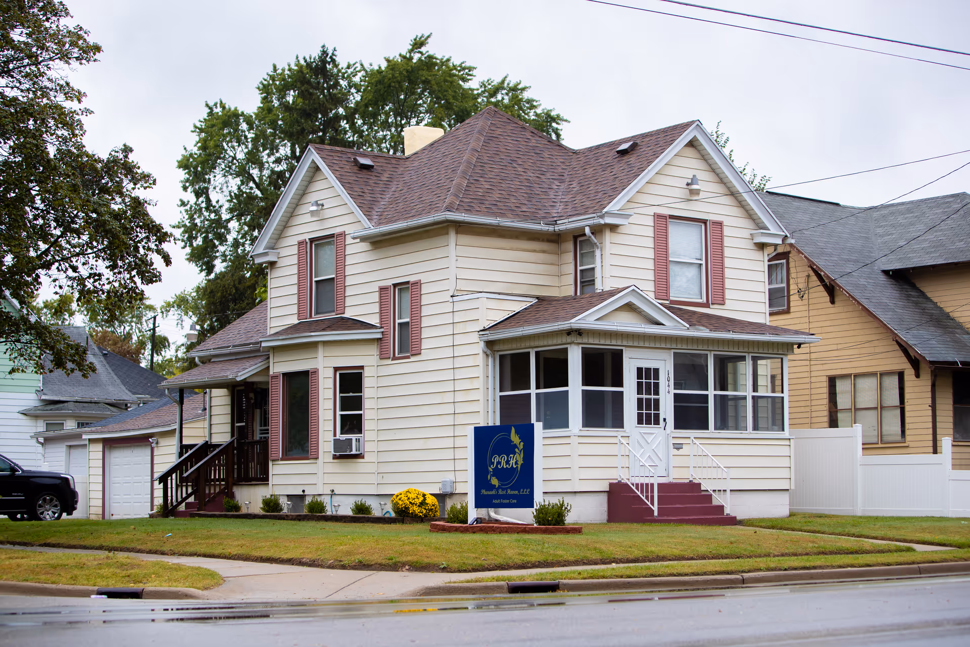 Two-story beige senior living facility with a front porch and a blue yard sign