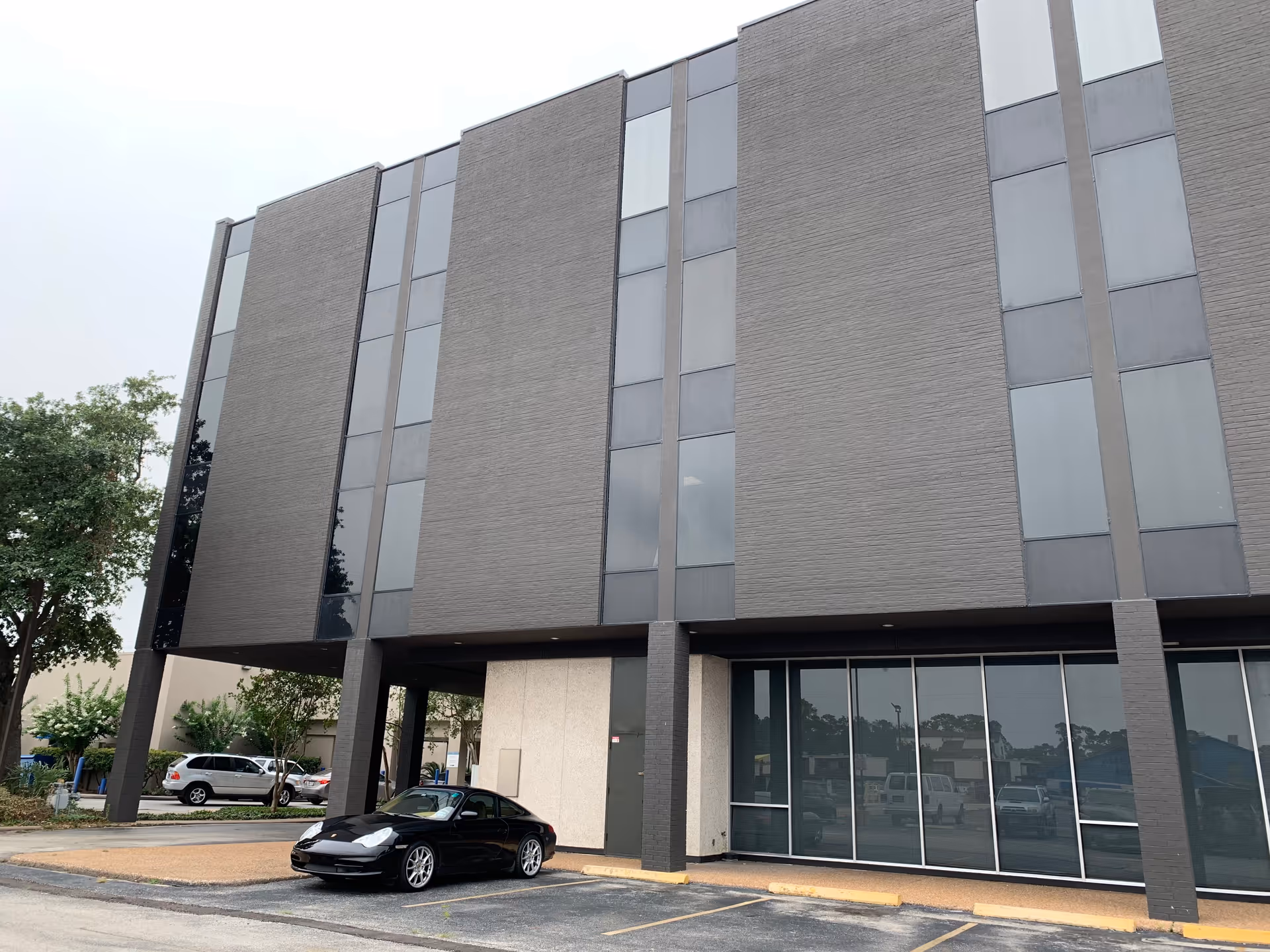 Modern gray brick building with tall windows and a black car parked in front.