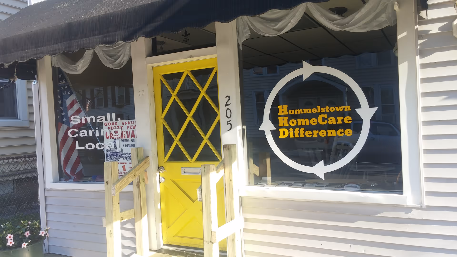Front of a light building with a bright yellow door and circular logo on the window.
