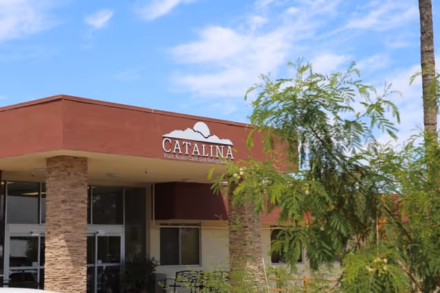 Front entrance of the Catalina Post Acute and Rehabilitation building with a covered portico, stone columns, and trees in the foreground.