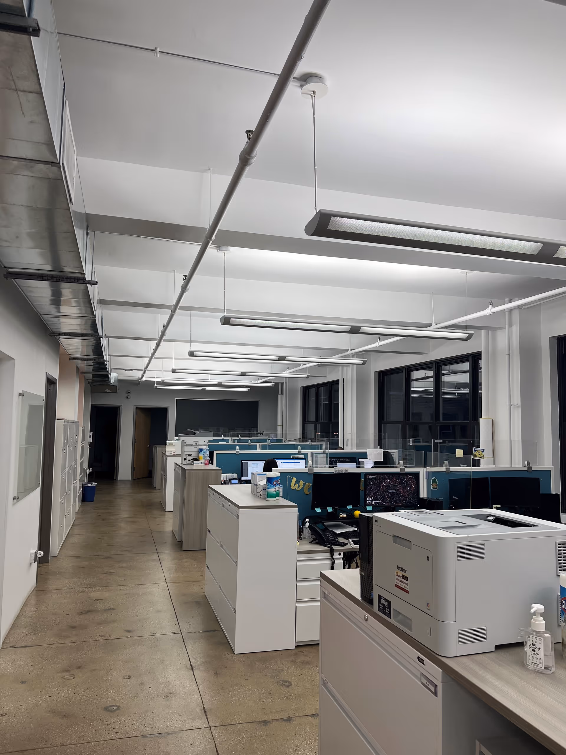 Open indoor office space with cubicles, desks, printers, and filing cabinets.