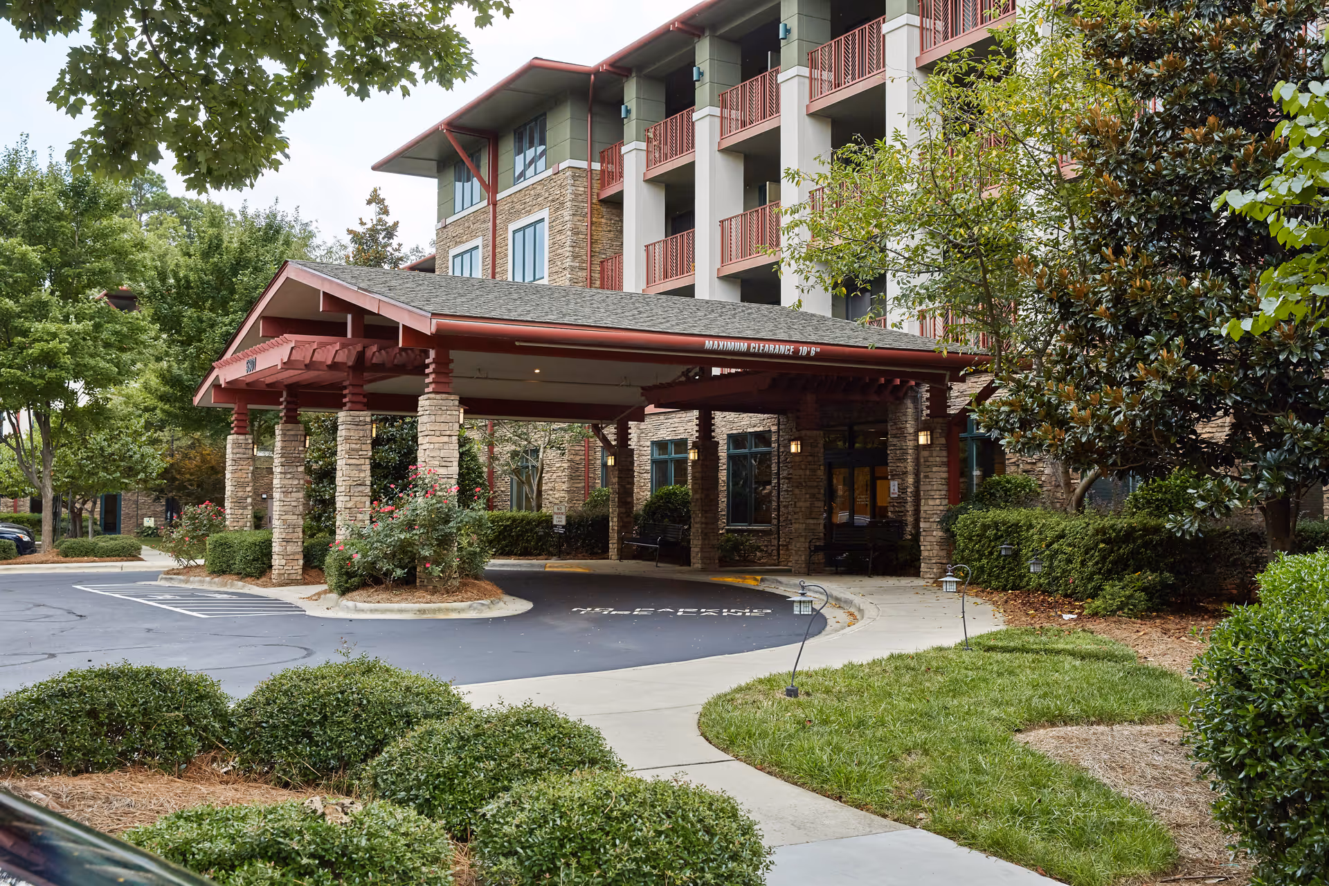 Covered porte-cochere entrance of Magnolia Glen with stone columns, balconies above, and landscaped driveway.