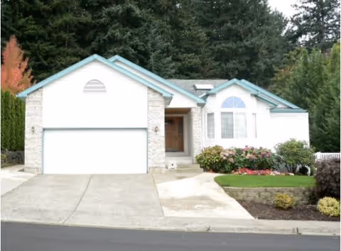 Single-story white house with an attached two-car garage, landscaped front yard, and trees in the background.