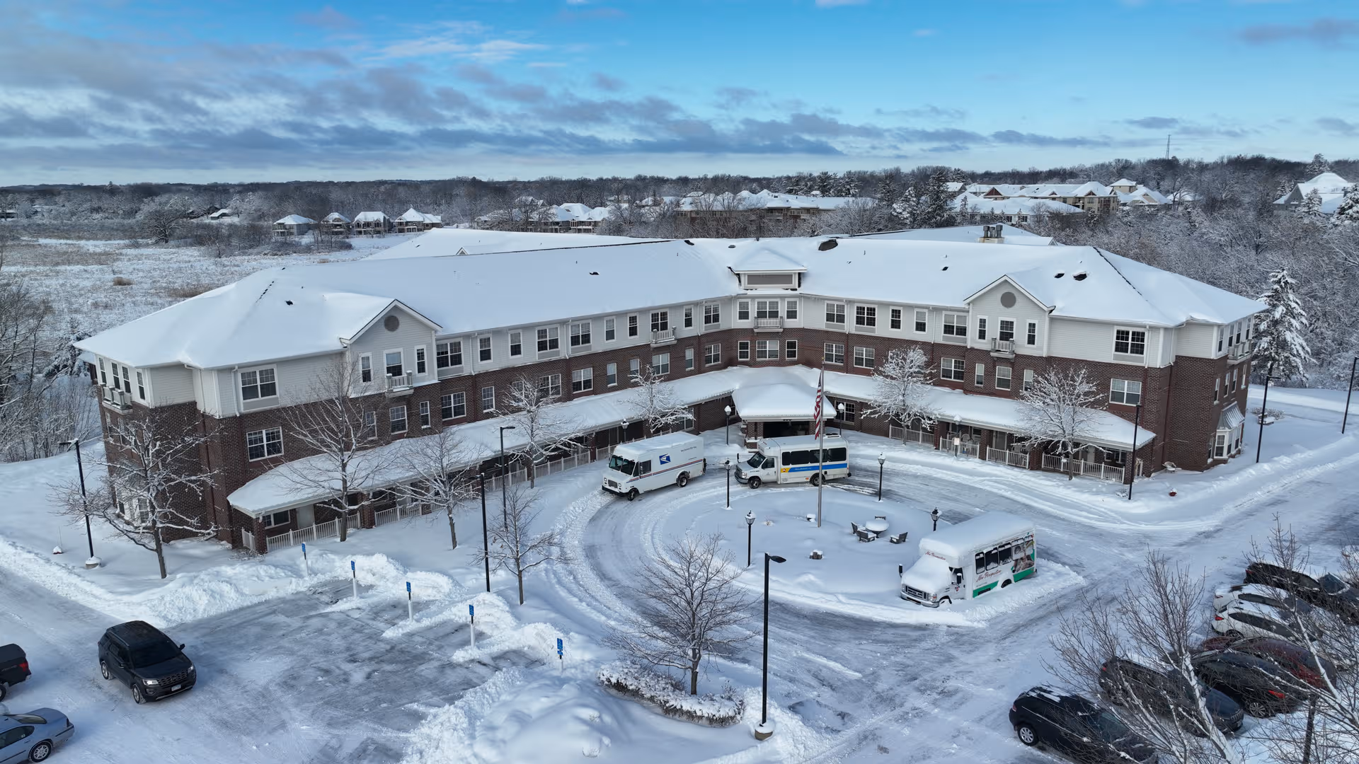 Snow-covered senior living facility with a circular driveway and buses in front.