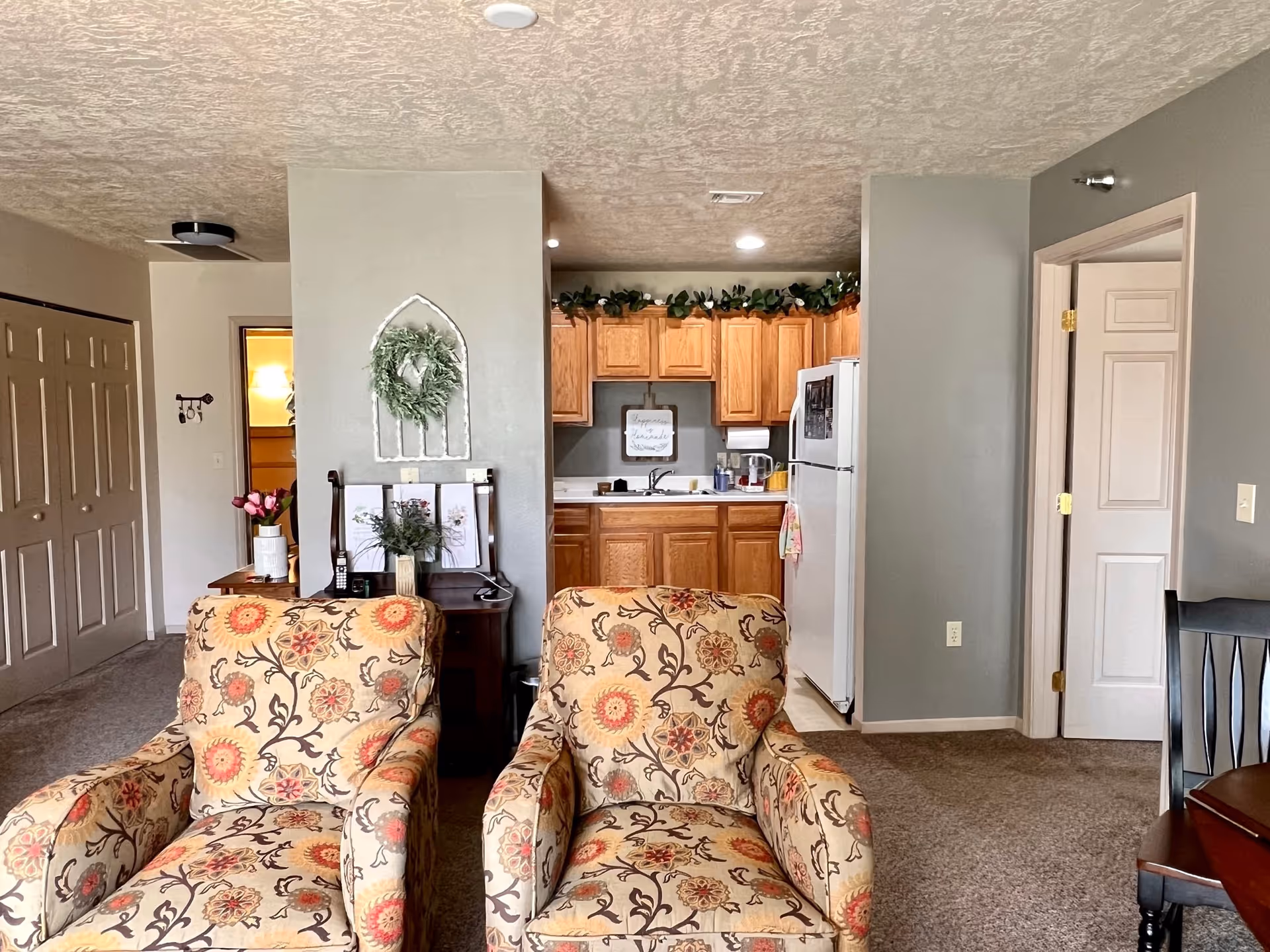 Two floral armchairs in a living area with a kitchenette visible in the back