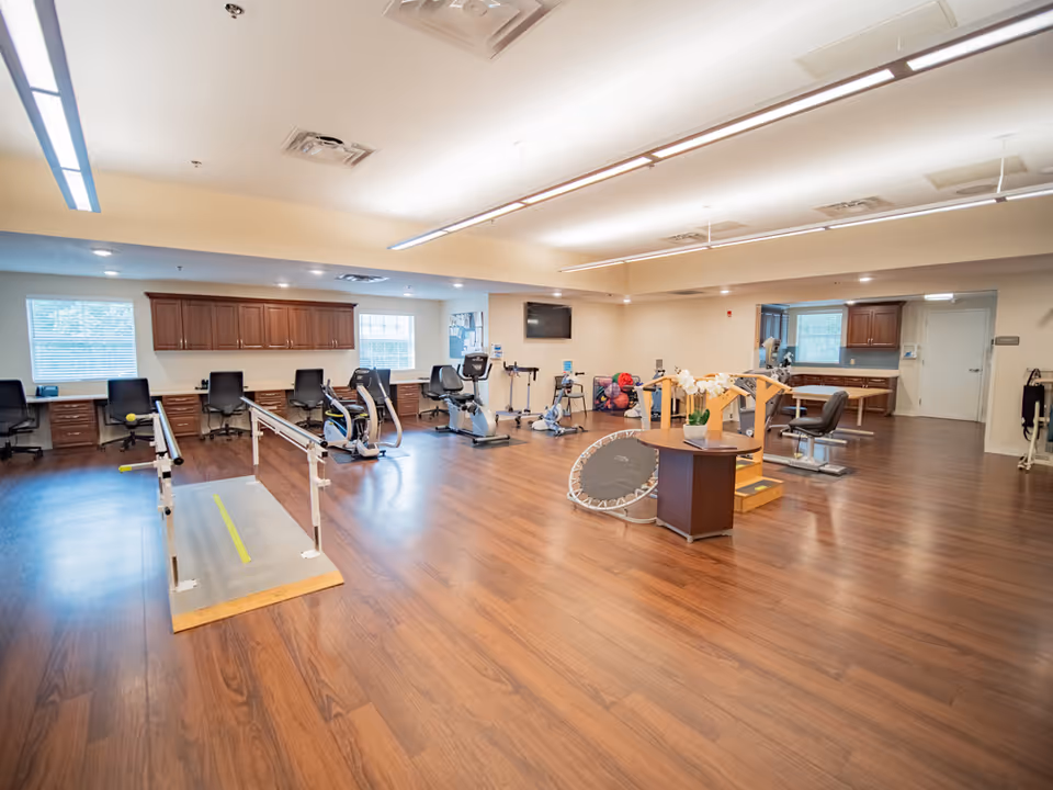 Spacious interior fitness room with gym equipment and wooden flooring.