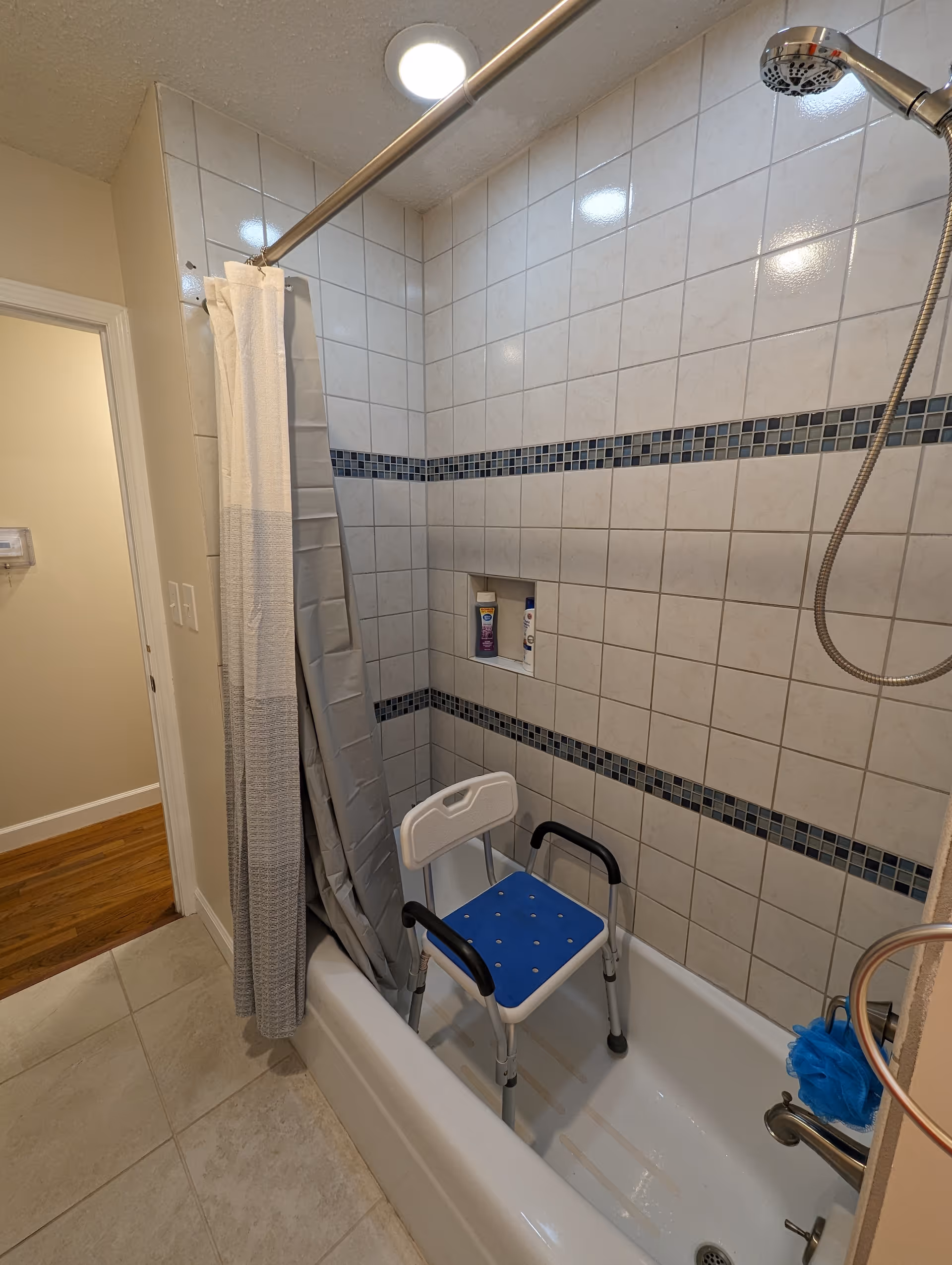 Accessible bathroom with shower, curtain, and blue shower chair inside tiled tub area.