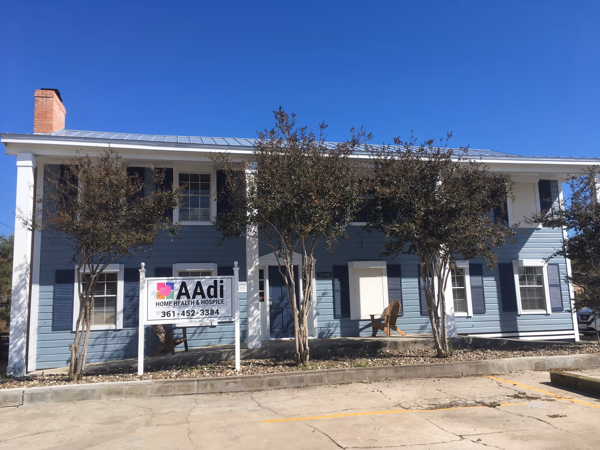 Blue, two-story building with an AAdi Home Health and Hospice sign and surrounding trees.