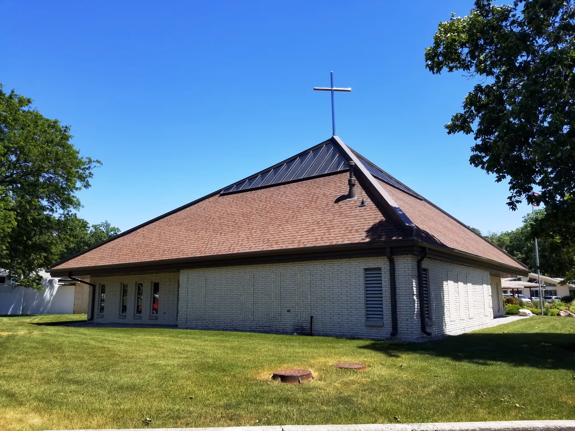 A brick building with a steep roof and cross on top sits on a green lawn.