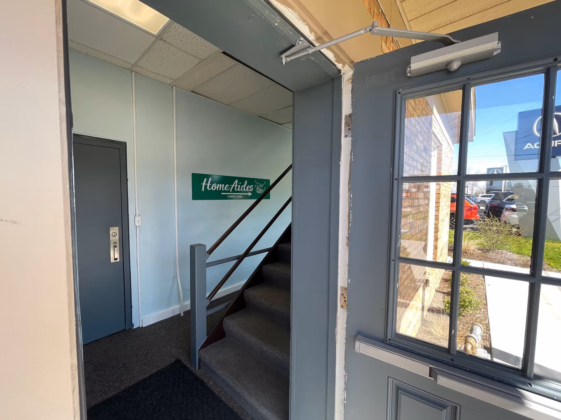 Interior stairwell at HomeAides facility with sign, stairs, door, and window.