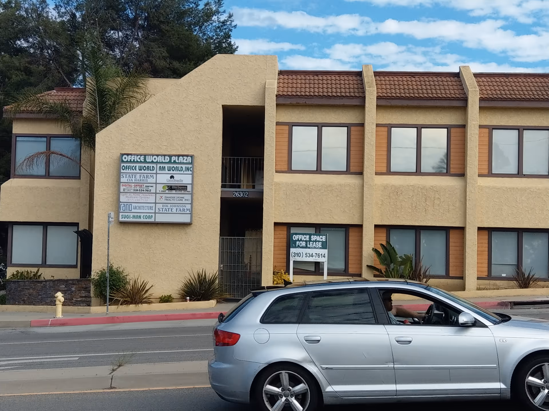 Beige two-story building with large windows and a parked silver car in front.