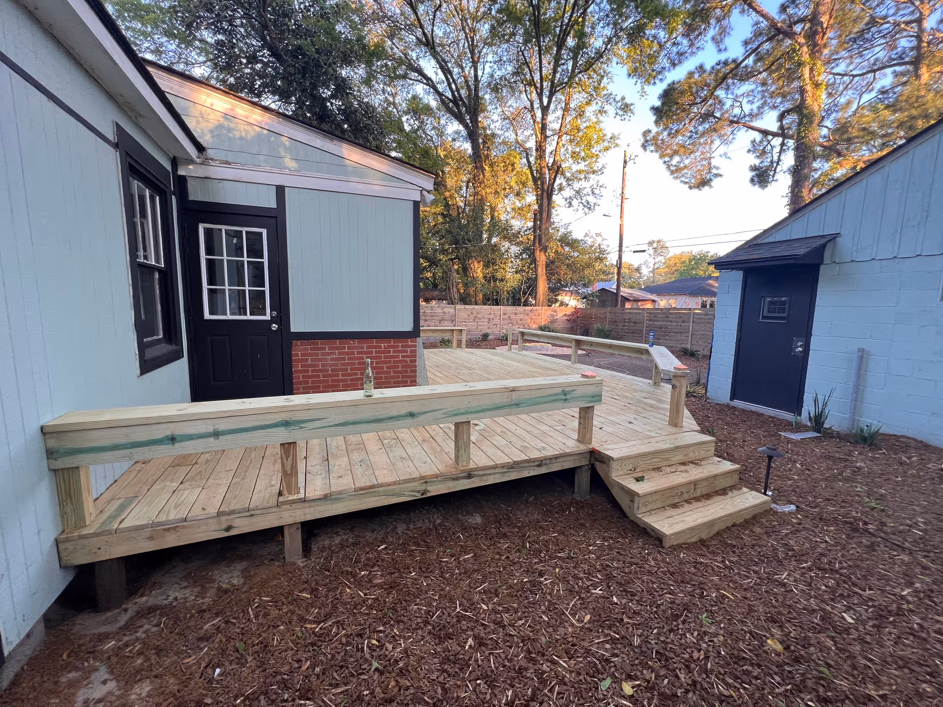 Wooden deck and steps extend from a light blue building featuring a black door.