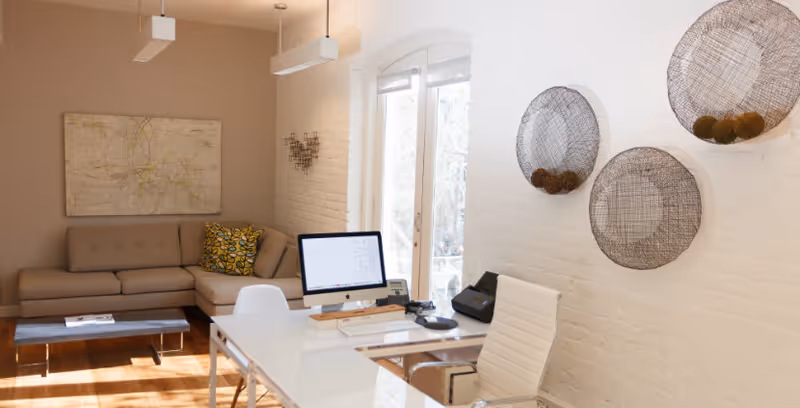 Bright interior office area with desk, computer, white chairs, and beige sofa.