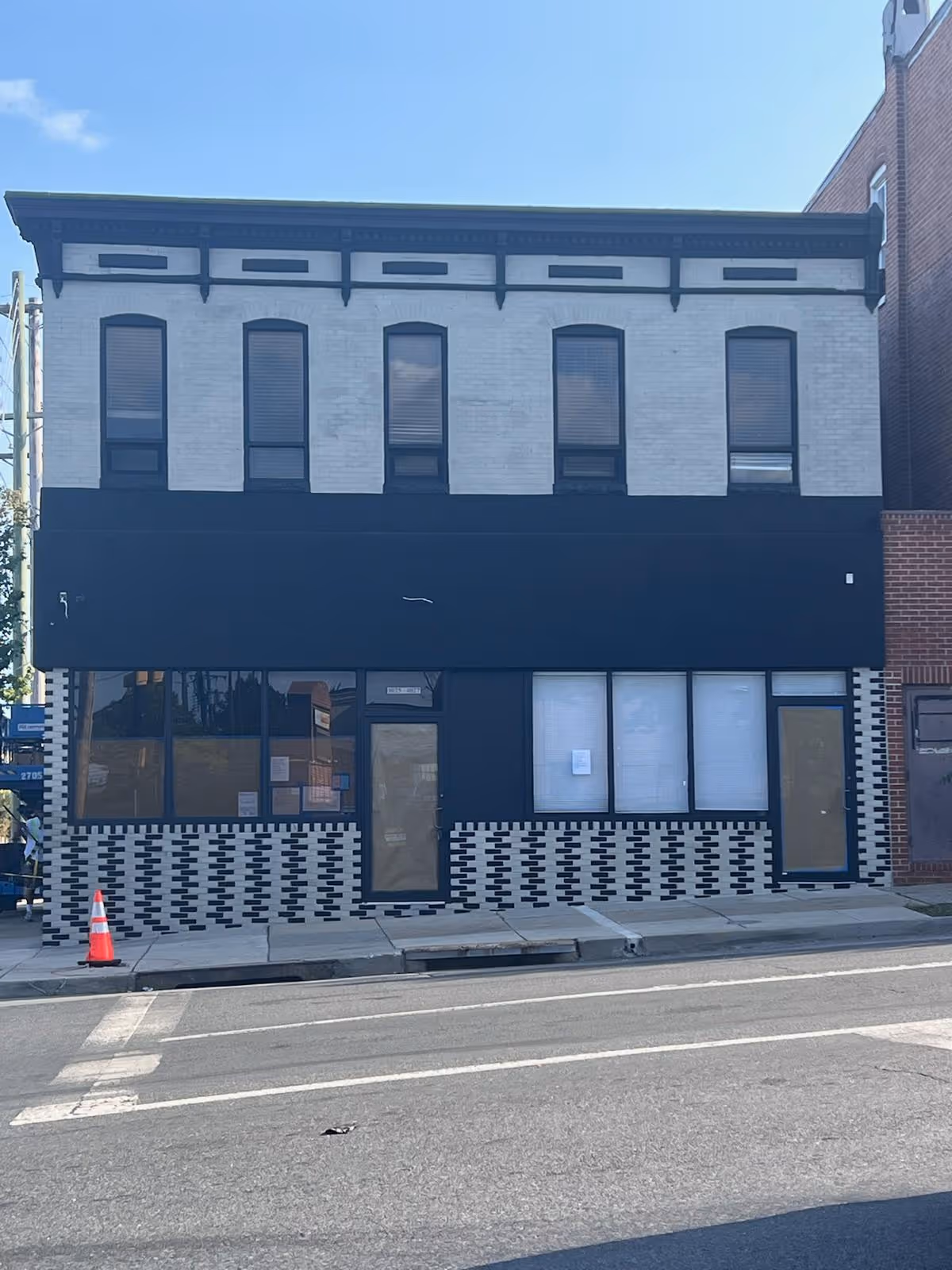 Two-story brick building with a black storefront and large street-facing windows.