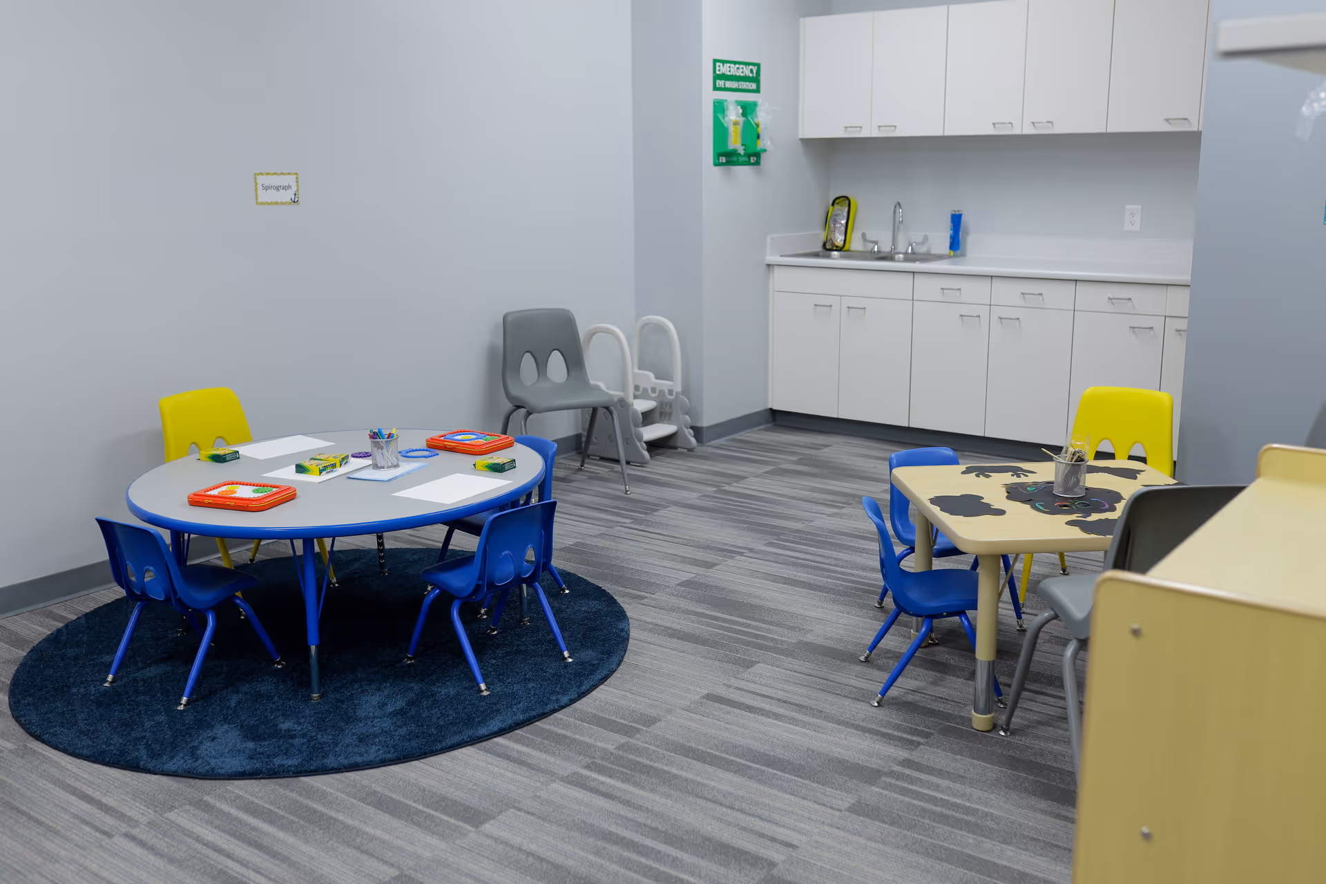 Interior play room with child-sized tables and chairs, kitchenette, and learning materials.