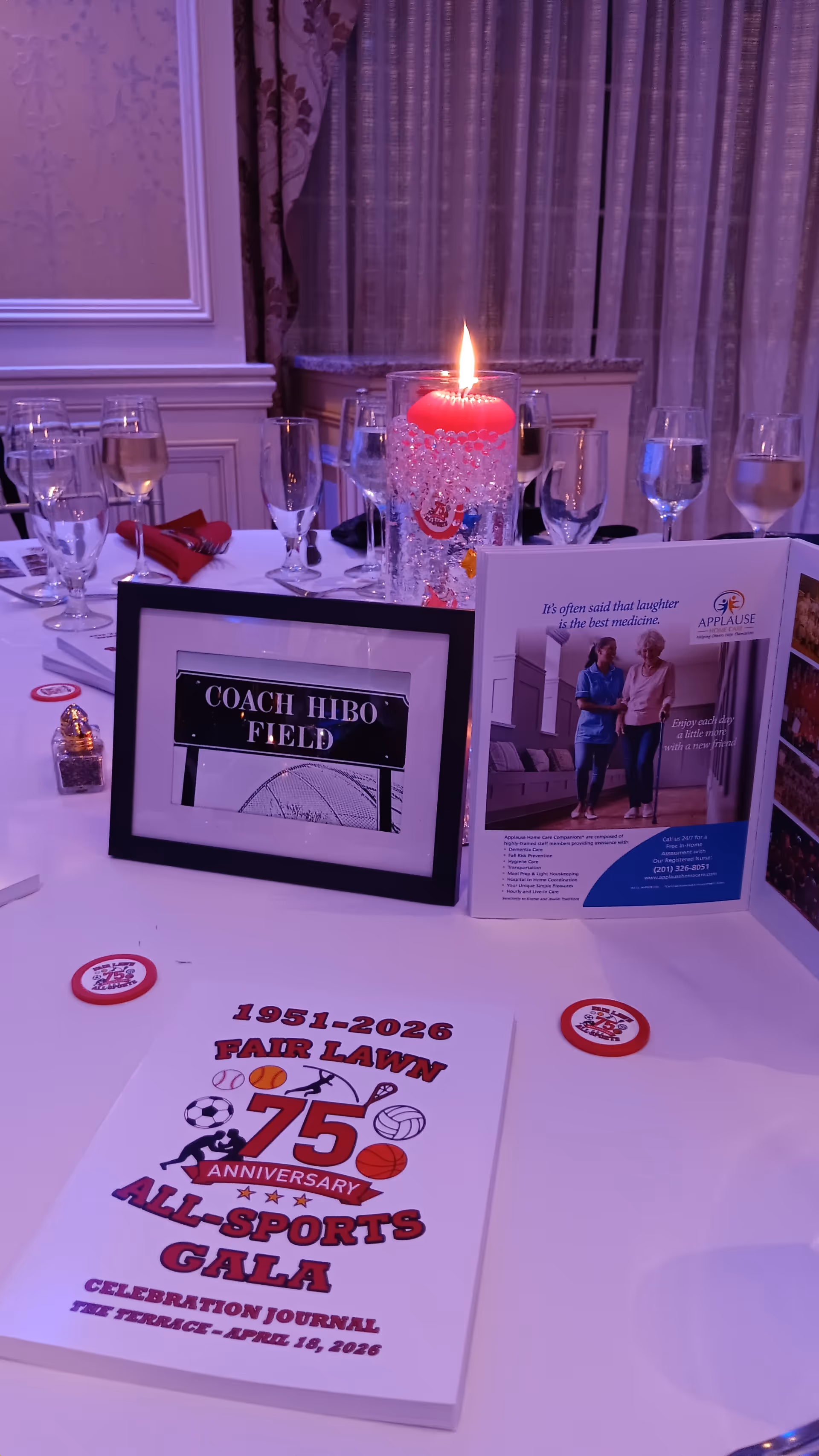 Indoor dining table set for an event with glassware, candle, and promotional materials.