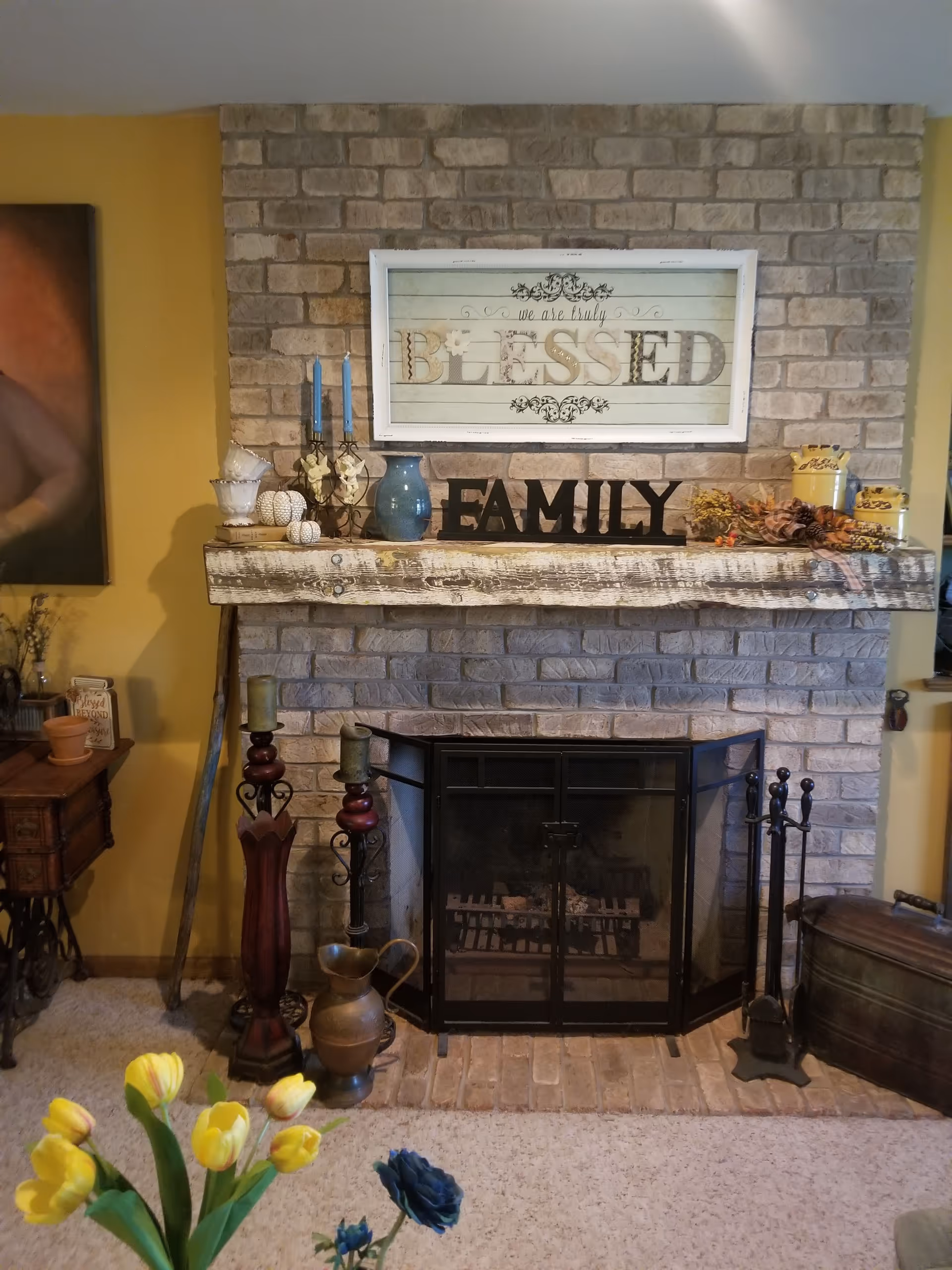 Cozy living room with brick fireplace, rustic mantle decor, and a framed Blessed sign.