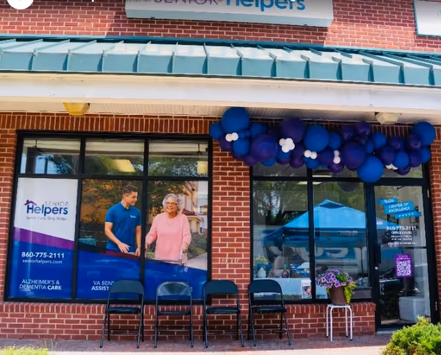 Exterior view of Senior Helpers storefront with purple blue balloons and chairs outside.